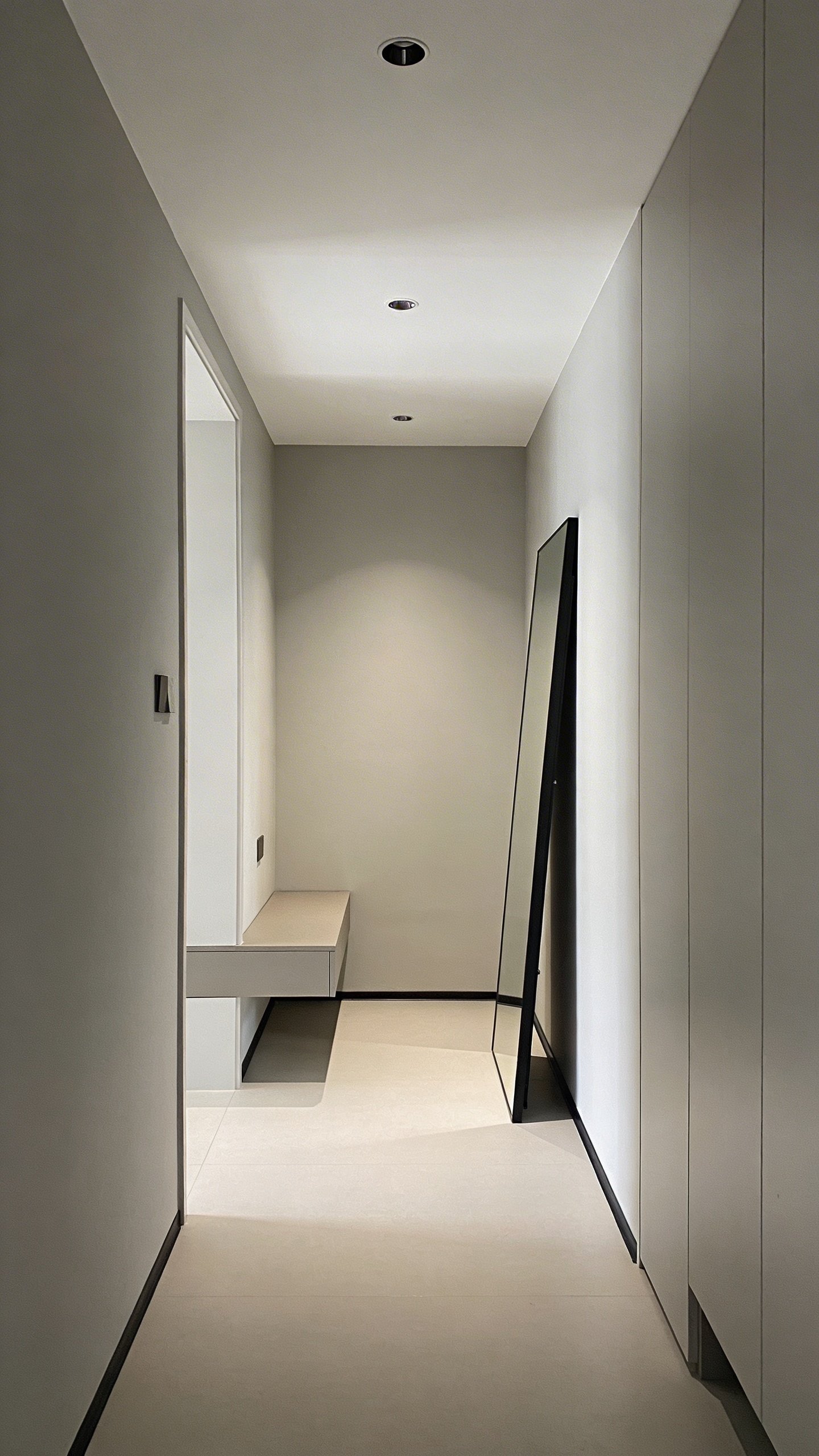 A minimalist hallway transition: furniture-free walking path with a slim hallway console near the entry, a tall mirror to visually enlarge the space, and soft ambient lighting, showcasing an uncluttered flow between rooms.